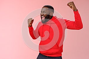 Extremely happy bearded young 25s black guy triumphing happily yelling yeah raising clenched fists celebrating success