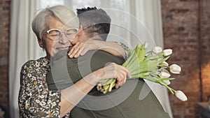 extremely happy caucasian grandmother hugs her grandson and holds white tulips bouquet on grandparent& x27;s day