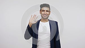 Extremely happy friendly man in suit waving hand looking at camera with smile, glad to see you, saying hi or good bye