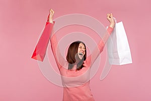 Extremely happy satisfied woman with brown hair in pink sweater rising hands with shopping bags, celebrating good holiday sales
