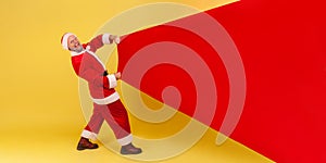 Extremely happy smiling elderly man with gray beard wearing santa claus costume pulling huge bag of gifts, copy space for