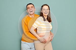 Extremely happy smiling joyful cheerful family waiting baby  over blue background hugging each other expressing love