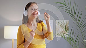 Extremely happy woman having fun at home dancing and listening to music in headphones moving happily enjoying relaxed weekend