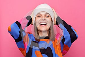 Extremely happy young adult Caucasian woman with brown hair wearing sweater posing isolated over pink background, standing with