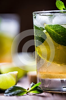 Extremely nice composition of Mojito half glass macro with mint and lime on the wooden table. Blurred background