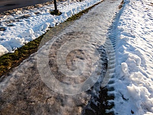 Extremely slippery footpath covered with melting snow and visible frozen ice footprints after heavy snowing in city in winter.