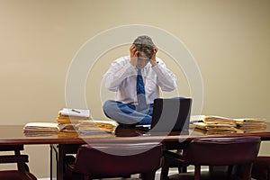 Extremely stressed out upset overworked man at work sitting on table with stacks of project folders photo