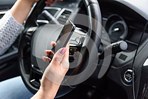 Extremely unsafety driving. Young woman in jeans and blue sweater is driving the car with one hand, using her smartphone by