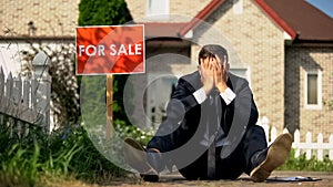Extremely upset real estate manager sitting by for sale signboard, failed deal