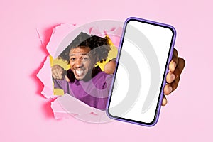 Exuberant man with curly hair joyfully pointing through a ripped pink paper, holding a smartphone