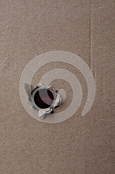 Eye of the camcorder looks through a torn hole in an empty brown cardboard, craft paper, concept of secrecy, covert video