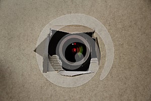 Eye of the camcorder looks through a torn hole in an empty brown cardboard, craft paper, concept of secrecy, covert video