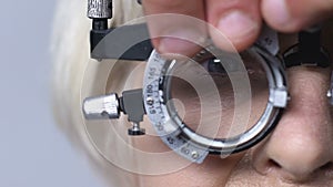 Eye doctor changing lenses in phoropter, checking mature patient vision, closeup