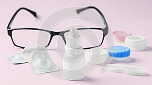 Eye dropper with contact lens, eyeglasses and accessories on pink background