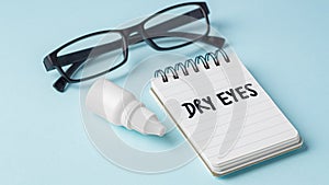 Eye drops and eyeglasses with dry eyes word on notebook on blue background