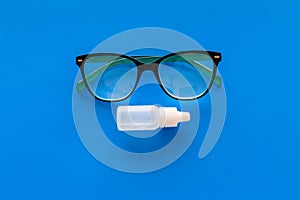 Eye drops in small bottle near glasses on blue background top view copy space