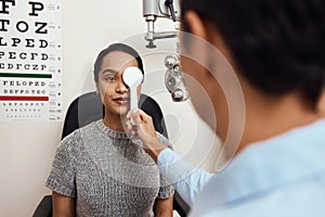 Eye exam, vision testing at an optometrist with young woman and doctor. Opthamologist using an occluder to test eyesight