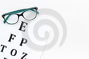 Eye examination. Eyesight test chart and glasses on white background top view space for text