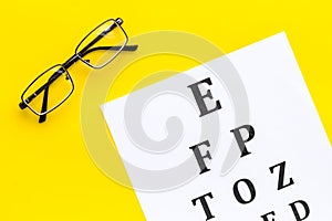 Eye examination. Eyesight test chart and glasses on yellow background top view copy space