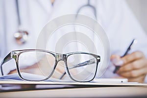 Eye glasses on desk with blur background of doctor writing prescription