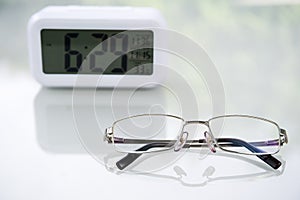 Eye glasses and Digital clock on table at home