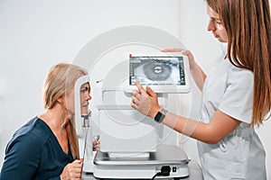 Eye is on the monitor. Woman`s vision is tested by clinic worker that using special device