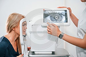 Eye is on the monitor. Woman`s vision is tested by clinic worker that using special device