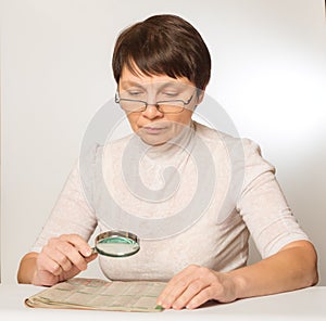 Woman with glasses and a magnifying glass reading a newspaper