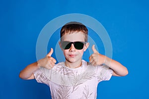 eye protection from the sun. child boy in sunglasses show thumb up on light blue studio background