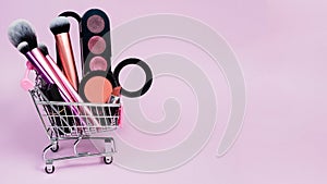 Eye shadow blush, lipstick and various makeup brushes in a pink trolley of the buyer. The concept of online shopping decorative