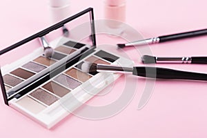 Eye shadow palette and makeup brushes on pastel pink background