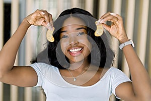 Eye skin antiwrinkle treatment. Smiling African American woman in white t-shirt, holding golden patches for skin under