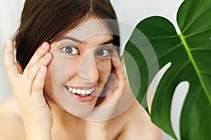 Eye Skin Care and Treatment. Portrait of beautiful young happy woman holding hands at eyes skin at green palm leaf. Girl enjoying