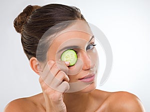 Eye treatment, homestyle. Portrait of a gorgeous young woman holding a slice of cucumber over her eye.