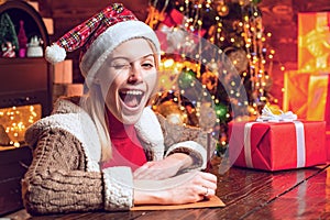 Eye winking blonde beautiful woman in Santa hat at Christmas home.