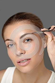 Eyebrow Correction. Beautiful young woman tweezing eyebrows. Model with beauty face