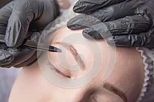 Young woman plucking eyebrows with tweezers close photo