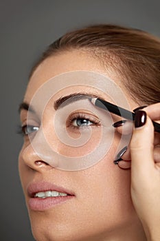 Eyebrow makeup. Beautiful model shaping brows with brow pencil closeup. Beauty woman with professional makeup contouring eyebrows.