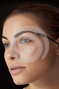 Eyebrow makeup. Beautiful woman shaping brows with eyebrow brush closeup.