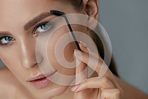 Eyebrow makeup. Woman brushing brows with gel brush closeup photo