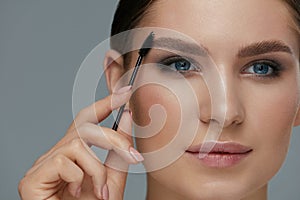 Eyebrow makeup. Woman brushing brows with gel brush closeup