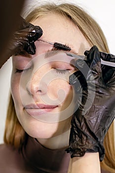 Eyebrow master using a set of tools combs and removes unwanted hairs with tweezers close-up on the client`s skin