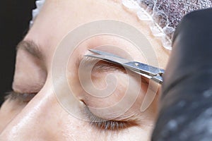 Eyebrow shaping in a beauty salon. the girl is trimmed with scissors for extra hair on her eyebrows.