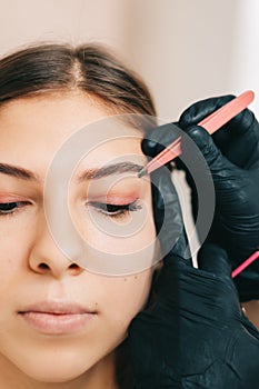 Eyebrow shaping procedure, make-up master uses tweezers and brush to shape the eyebrows