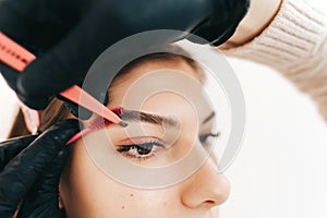 Eyebrow shaping procedure, make-up master uses tweezers and brush to shape the eyebrows