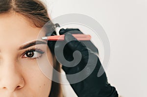 Eyebrow shaping procedure, make-up master uses tweezers to shape the eyebrows