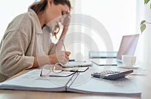 Eyeglasses and calculator close-up and tired accountant woman making marks in paper documents with modern laptop sitting