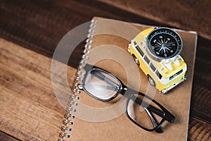 Eyeglasses, compass, book and toy miniature minivan on a wooden table.