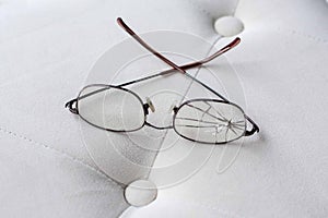 Eyeglasses with cracked lens on cream colored ottoman photo