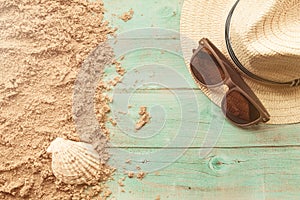 Eyeglasses and hat on wooden background with sand